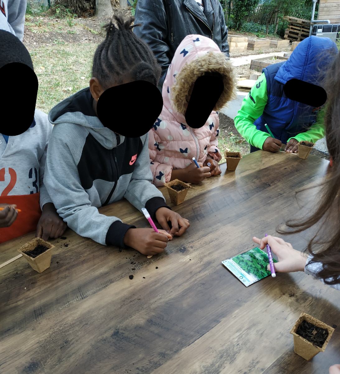 Une enfant écrivant son nom sur un bâtonnet à planter dans son pot de persil, pour le retrouver plus facilement !
